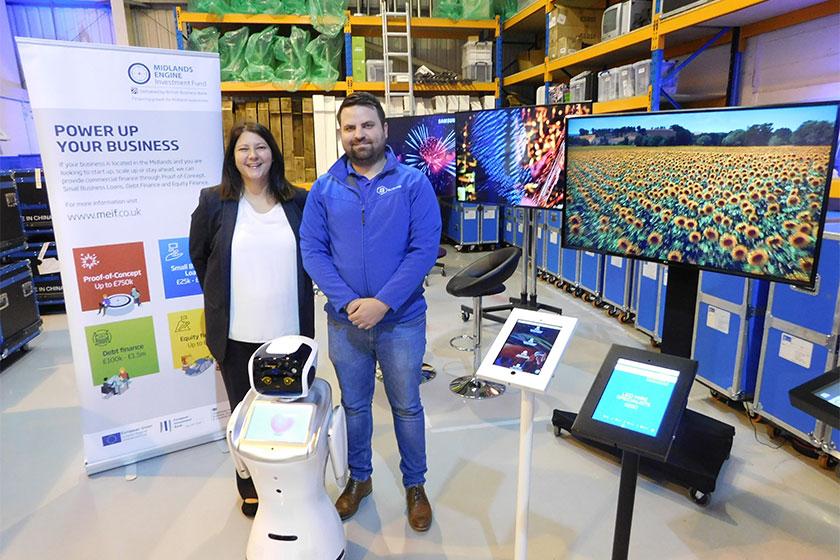 A man and a woman stood around TV screens in a warehouse with a MEIF pop up banner next to them