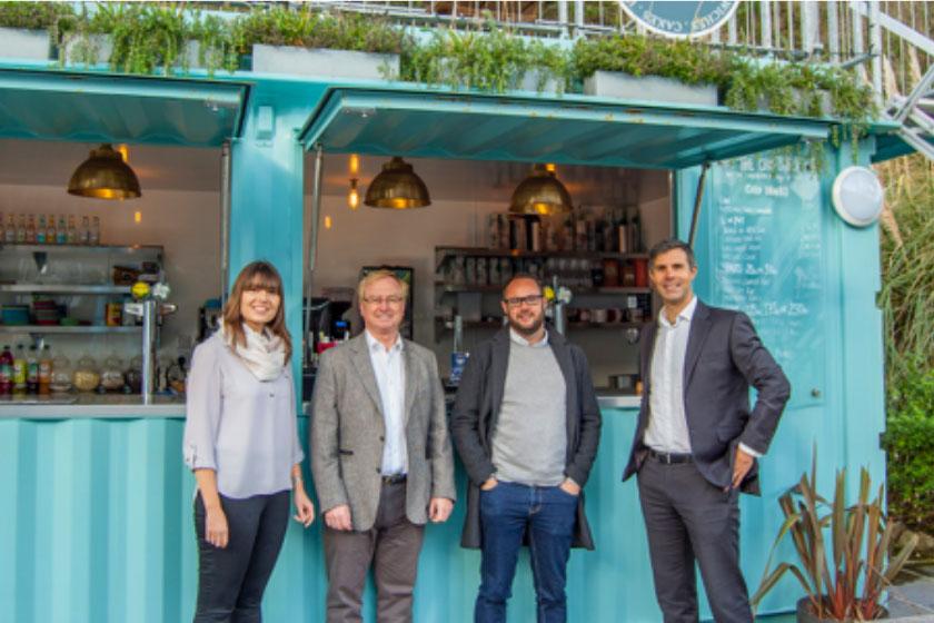 3 men and a woman smiling and stood in front of a food stall