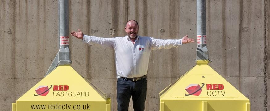 A man from Red Security Solutions stood with his arms out in between his solar powered security CCTV product