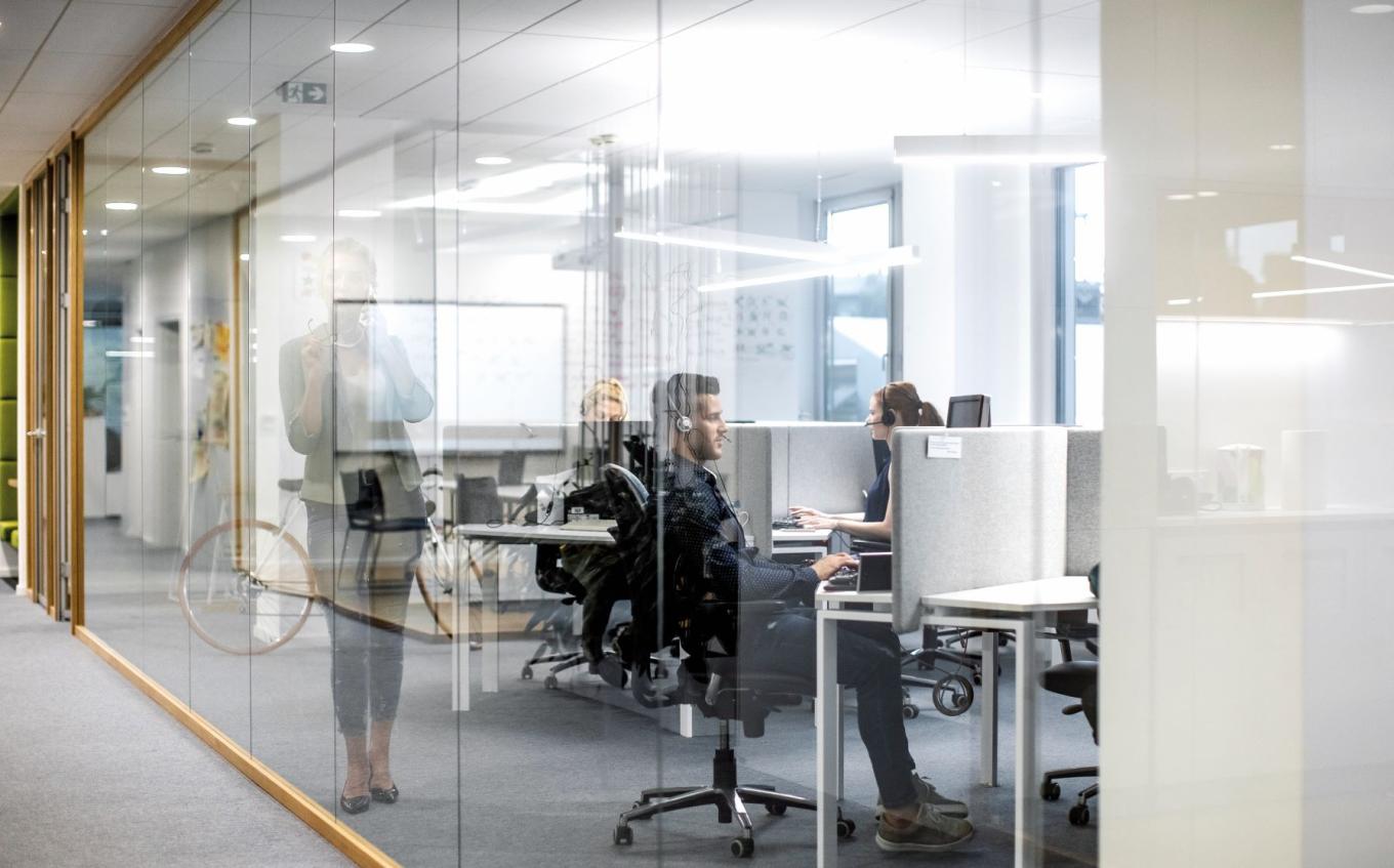 Interior of modern offices, with employees at desks wearing headsets and holding phone conversations with clients