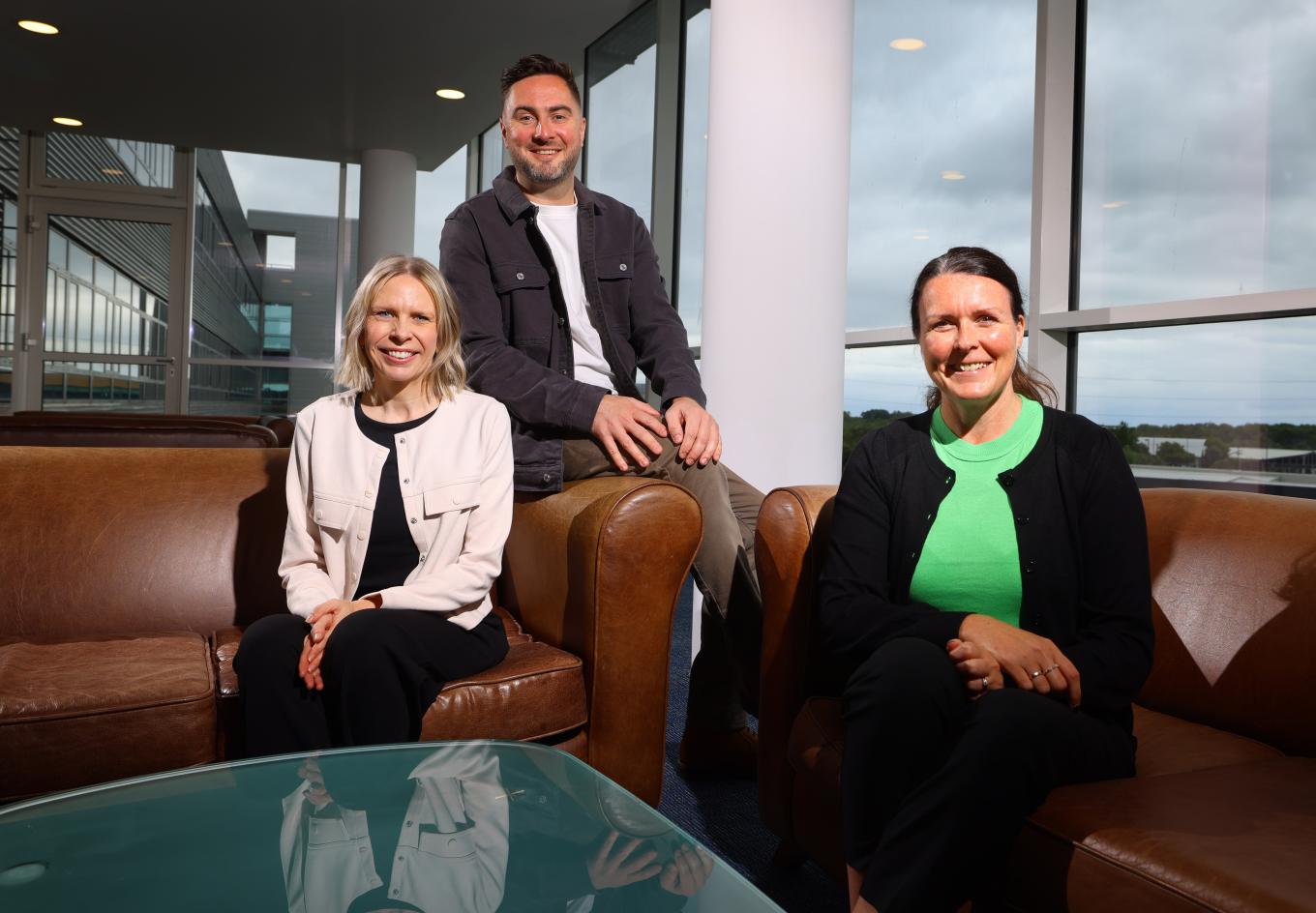 Two ladies and one man sitting on couches in a office lounge