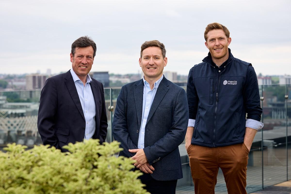 Three men standing on a rooftop overlooking a cityscape.