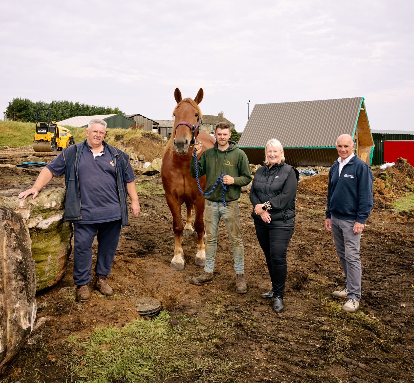 Four people standing on a farm next to a horse 