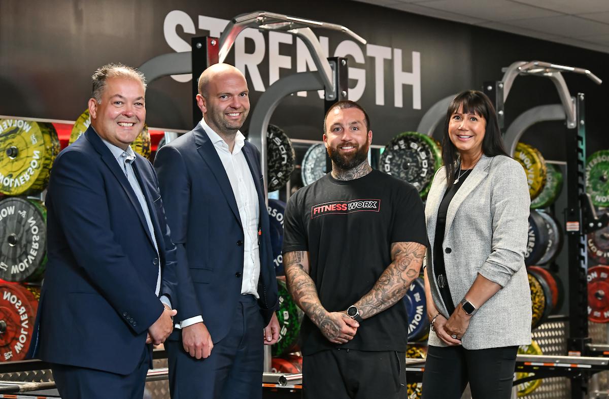 A group of three men and one woman stands together in a gym