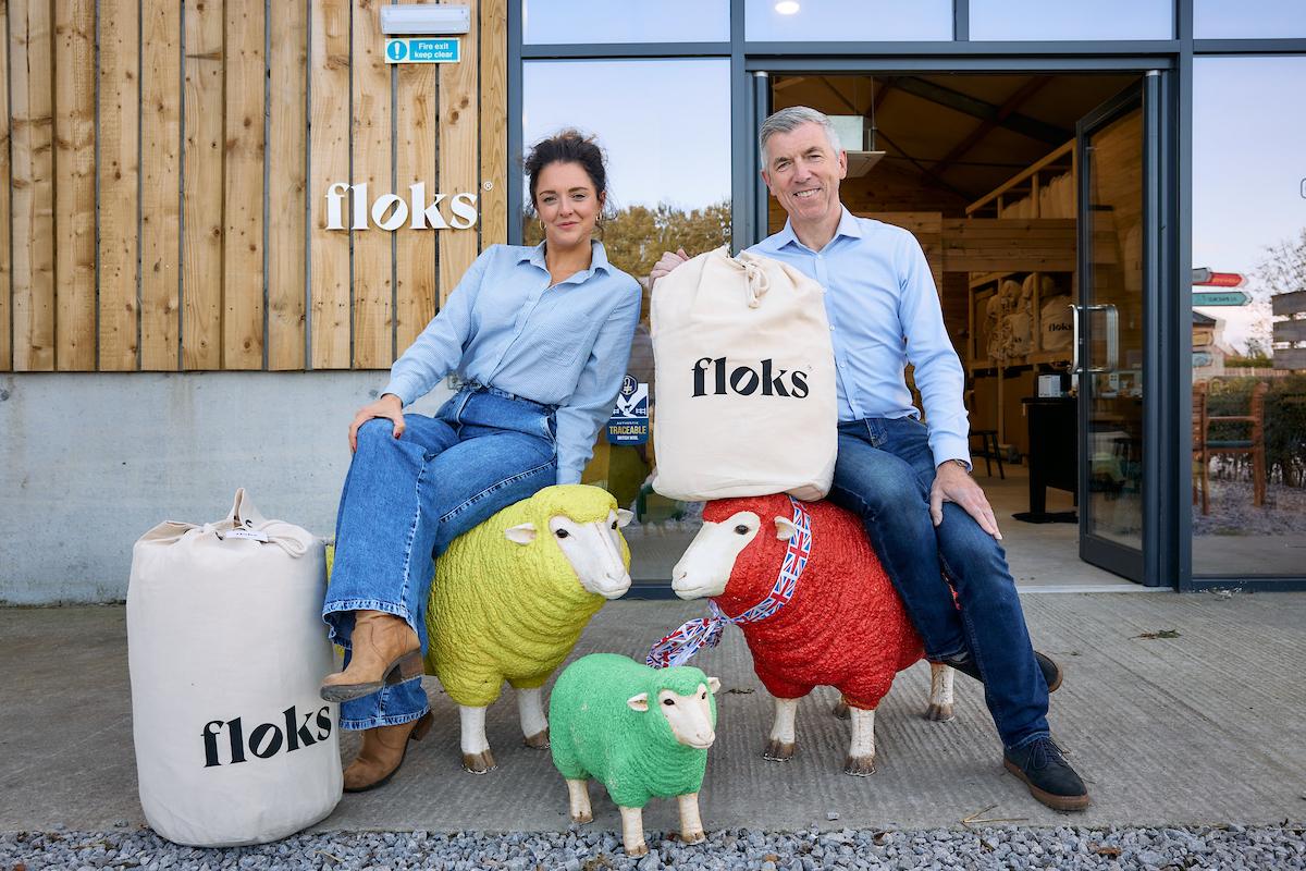 A man and a woman sitting on sheep ornaments with bags of wool