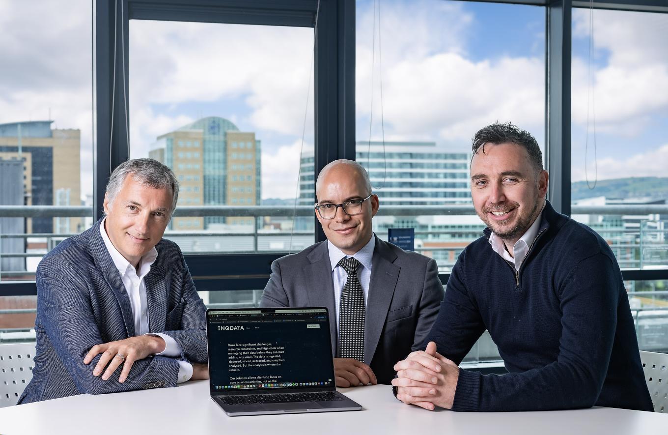 Photo of INQDATA CEO Theodore Voegt with Brian Cummings from Clarendon Fund Managers and Mark Sterritt from British Business Bank all sitting at a table in an office with Belfast in the background