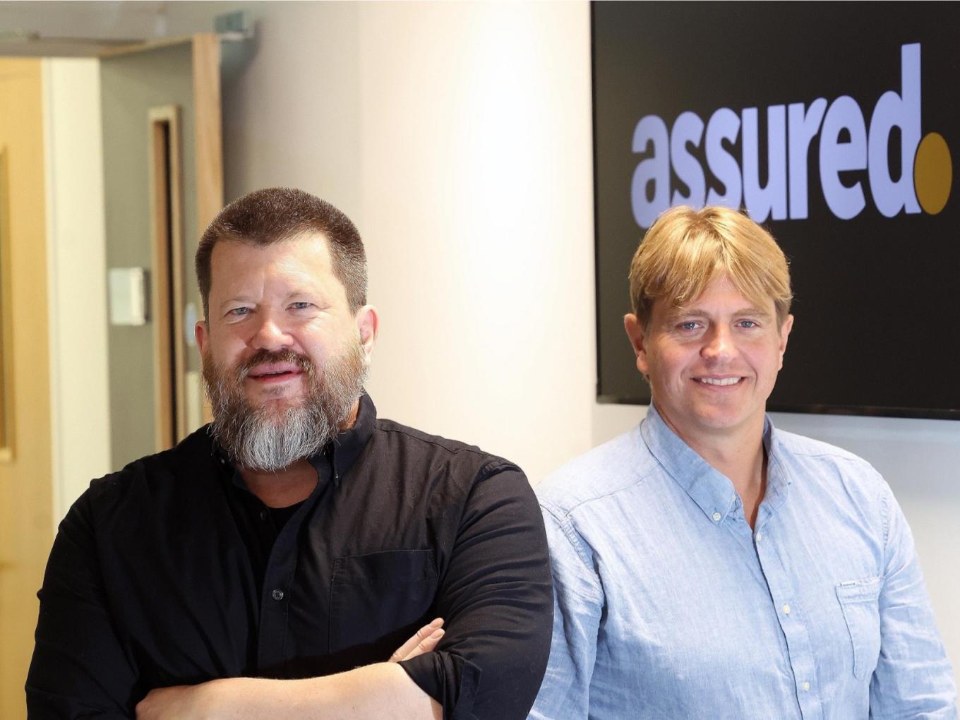 Photo of Assured Insights founders sitting in an office and smiling at the camera