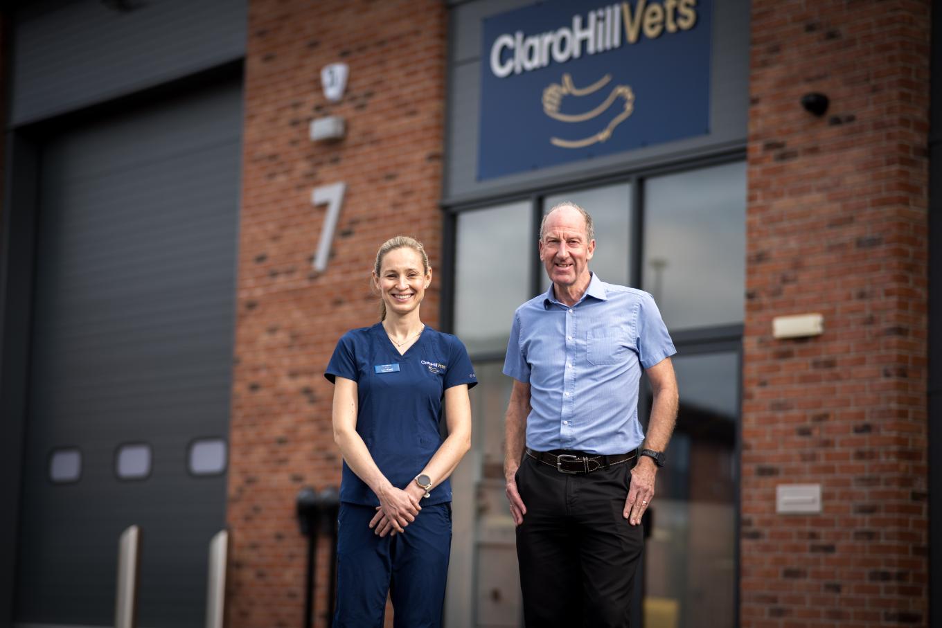 Two people pose in front of a structure marked with the sign "Claro Hill Vets"