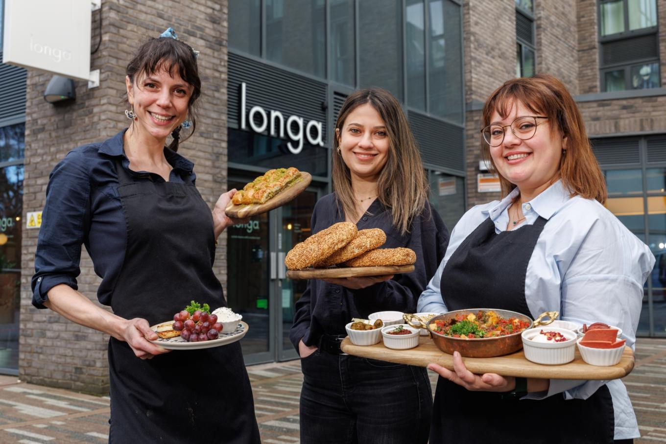 Photo of Longa Turkish cafe in Cardiff with owners Gizem Yorgun, Pinar Ogun and Simge Yalcin standing outside with plates of Turkish food