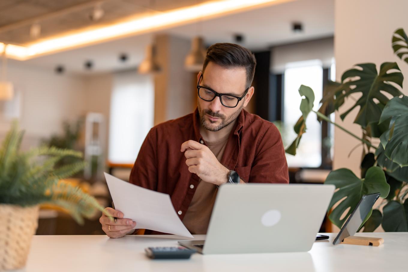 A male business professional reviewing a document sat at a desk in modern office environment