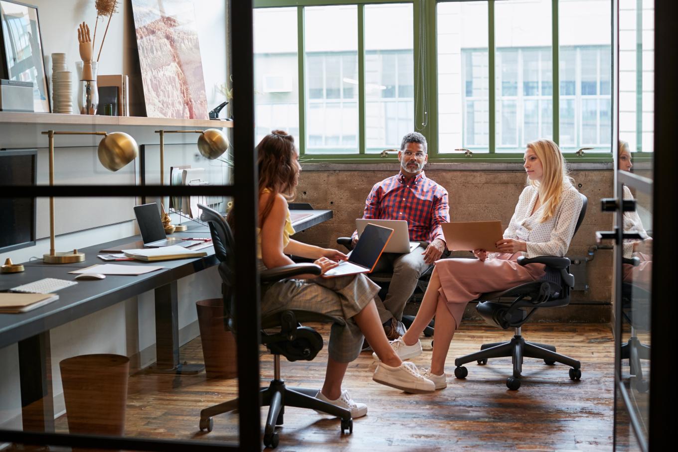 Two ladies and a gentleman sat relaxed in an urban loft style warehouse office